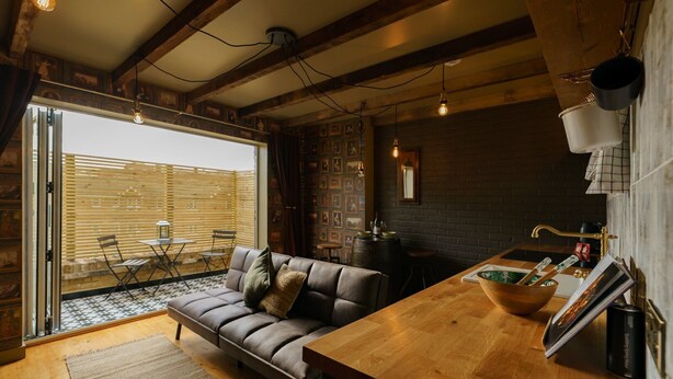 Un salon chaleureux avec un canapé en cuir, une table basse en bois et une table à manger. Il y a également un coin cuisine avec un mur en briques et un plan de travail en bois.