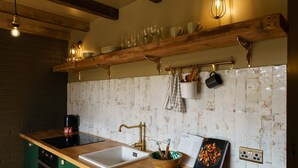 Une cuisine avec un plan de travail en bois, un évier blanc et un crédence ornée de carreaux à l’aspect vieilli. On y voit des ustensiles de cuisine suspendus et une machine à café posée sur le plan de travail.