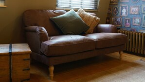 A brown leather sofa with a green pillow and a wooden chest of drawers in a room with wooden flooring and a radiator.