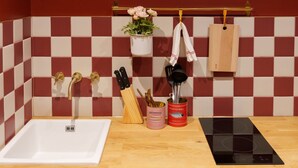 A kitchen with a white sink, wooden countertop, and a black induction cooktop. There are two gold faucets, a hanging plant, and a towel rack with a wooden cutting board.