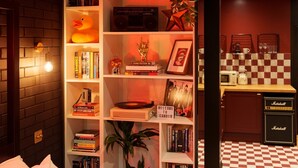 A cozy room with a bookshelf, a lamp, a plant, and a kitchenette area with a microwave and coffee maker.