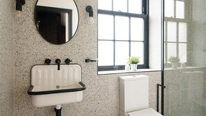 Un baño con un lavabo blanco, un espejo redondo y una ventana que ofrece vistas a edificios.