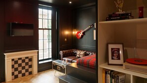Una habitación acogedora con chimenea de ladrillo visto, un sofá de cuero, una guitarra y una estantería con libros y un cuadro enmarcado.