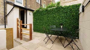 Un patio con una mesa y sillas, un portón de madera y un muro de seto verde.