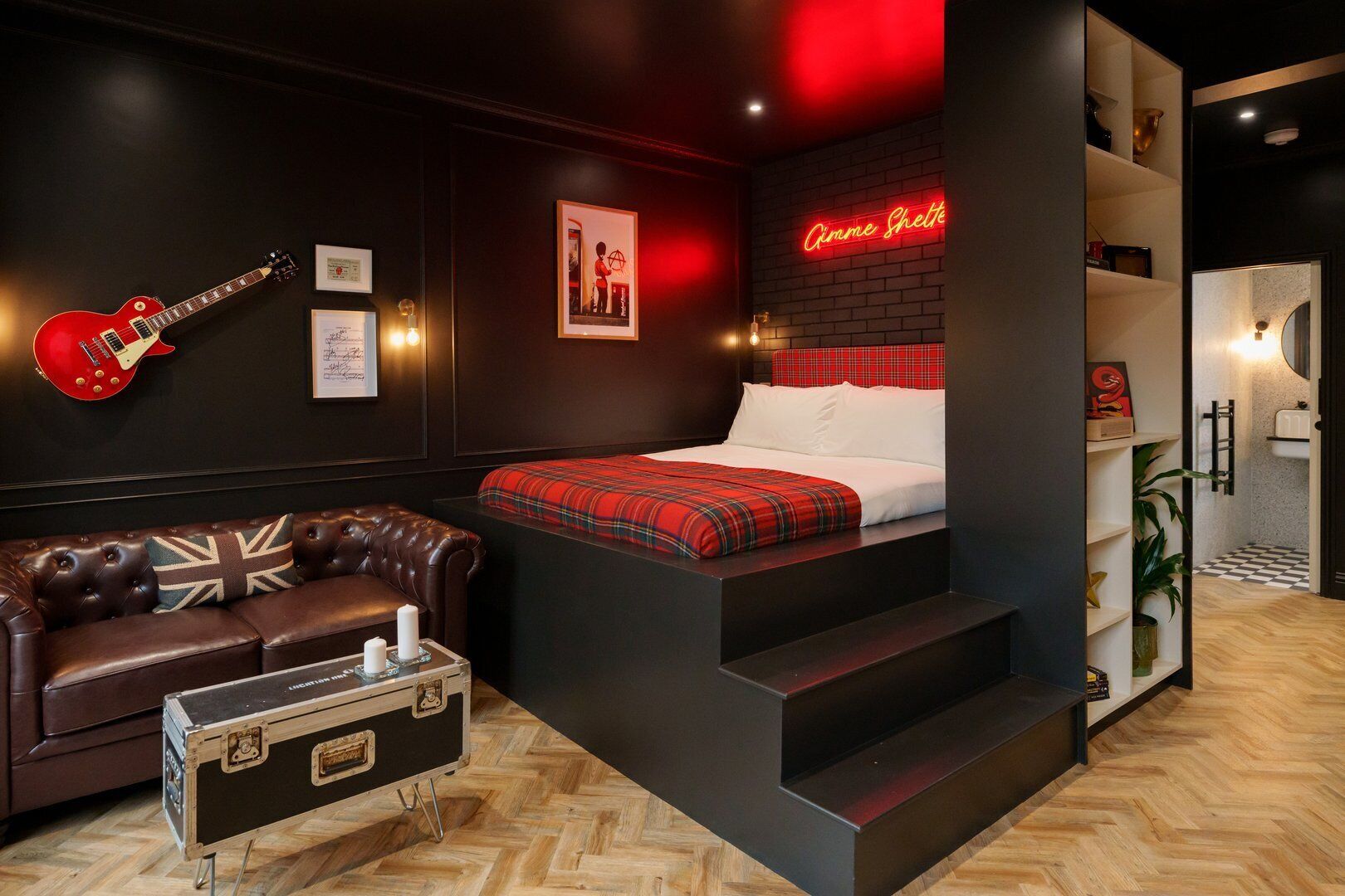 A modern bedroom with a red guitar, a plaid bedspread, and a neon sign reading "Aimee Schette".