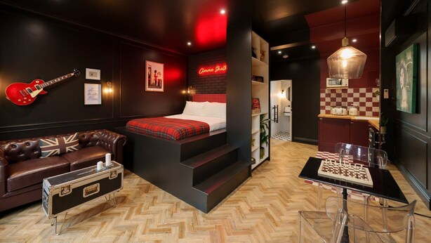 Una habitación moderna con cama, sofá de cuero, mesa de ajedrez y una guitarra.