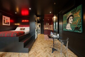 Ein modernes Hotelzimmer mit einem Bett, einer Essecke mit Tisch und Stühlen, einer Küche und einem großen Kunstwerk an der Wand.