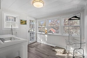 A bright laundry room with white walls, a wooden floor, and large windows.