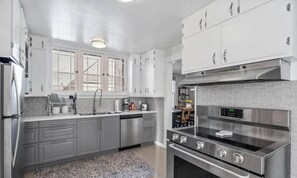 A modern kitchen with stainless steel appliances, grey cabinetry, and a patterned rug.