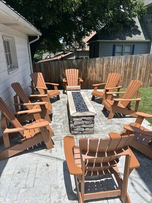 A patio with six Adirondack chairs arranged around a rectangular stone fire pit.