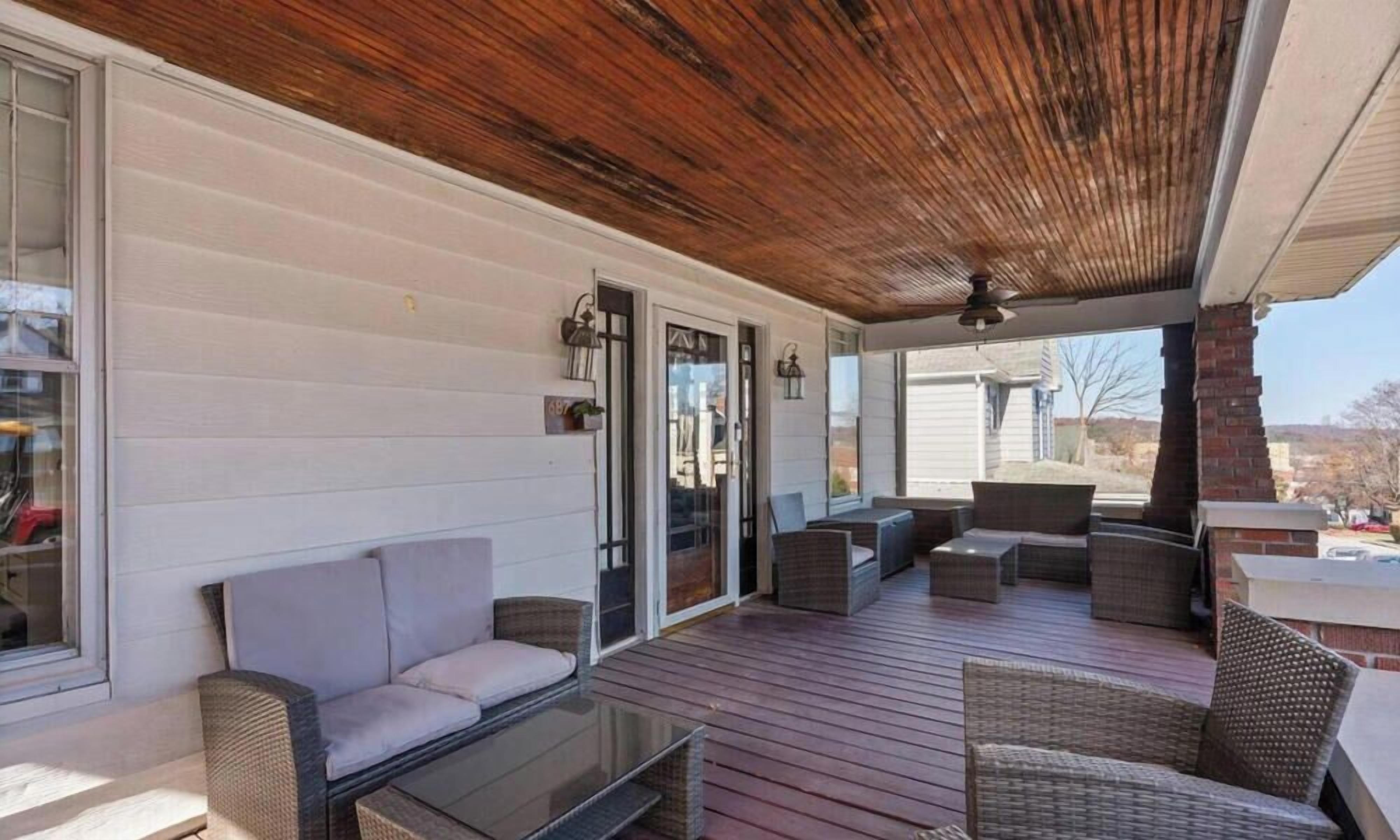 Une terrasse extérieure couverte, aménagée avec des meubles en osier, une table en verre et un plafond en bois.