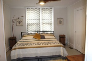 Une chambre à coucher avec un lit, une fenêtre ornée de rideaux à motifs et deux tableaux accrochés au mur.
