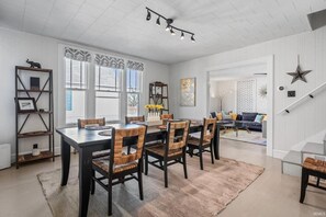 A dining area with a long table, six chairs, and a patterned rug.