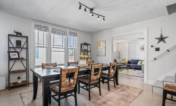 A dining area with a long table, six chairs, and a patterned rug.