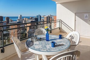 Ein Balkon mit Tisch und Stühlen, einer Blumenvase und Blick auf Stadt und Meer.