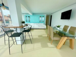 Uma sala de estar moderna com um sofá branco, uma mesa de jantar de vidro e cadeiras de metal preto.