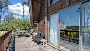 A wooden deck with outdoor furniture, a glass door leading to a balcony, and a view of trees and sky. - Cozy home biking distasnce from the beach by Seaside Vacations & Sales (Chincoteague Island)