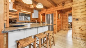 A wooden cabin interior with a kitchen featuring a stainless steel refrigerator, wooden bar stools, and pendant lighting. - Cozy home biking distasnce from the beach by Seaside Vacations & Sales (Chincoteague Island)