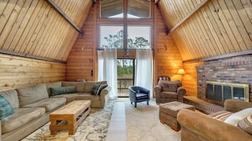 A cozy room with a wooden ceiling, a fireplace, a sofa, a chair, and a rug.