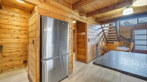 A wooden cabin interior with a kitchen area featuring a stainless steel refrigerator, a dining table with chairs, and a staircase leading to an upper level. - Cozy home biking distasnce from the beach by Seaside Vacations & Sales (Chincoteague Island)
