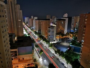 Paisagem urbana noturna com edifícios altos, uma rua bem iluminada e uma faixa de pedestres.