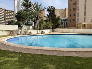 Uma piscina com um flutuador, cercada por palmeiras e um edifício com varandas.