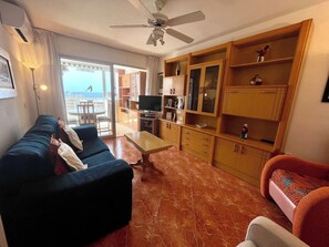 Uma sala de estar com sofá, televisão, armários de madeira e ventilador de teto.