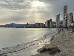 Una spiaggia con sullo sfondo la linea dell'orizzonte cittadina, con grattacieli e una catena montuosa.