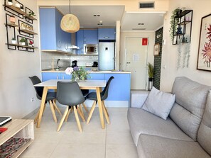 Una cucina moderna con mobili blu, un tavolo da pranzo con sedie e un divano grigio in zona soggiorno.
