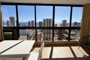 Um quarto com uma janela grande, uma mesa, duas cadeiras e uma cadeira preta.