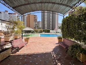 Un espacio al aire libre techado con piscina, bancos y plantas en macetas.