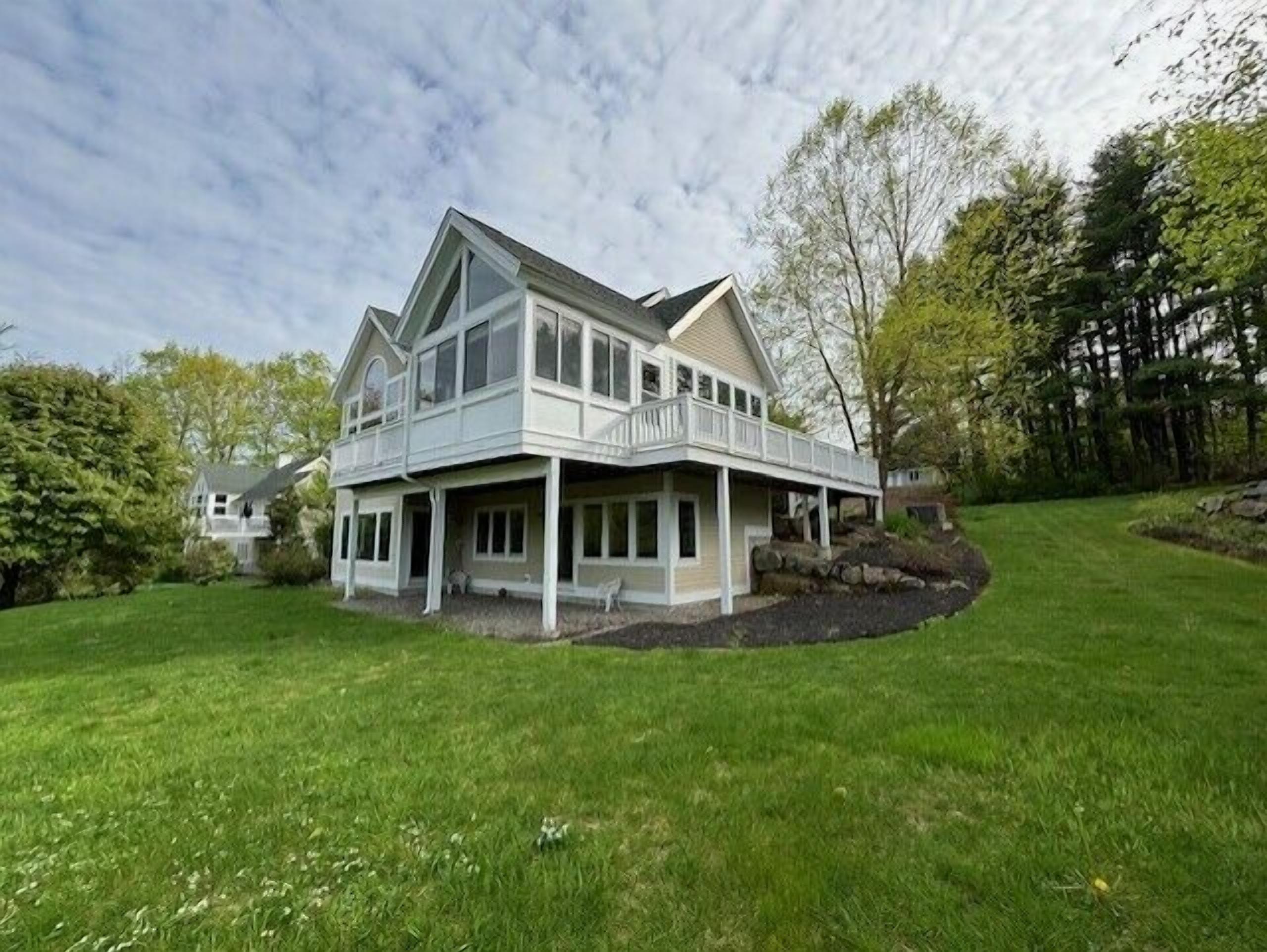 A two-story house with a balcony, surrounded by a well-maintained lawn and trees.