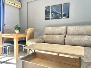 Uma sala de estar moderna com um sofá, uma mesa de jantar de madeira e um vaso com planta.