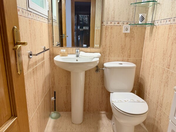 A bathroom with a pedestal sink, toilet, and a glass shelf above the sink.