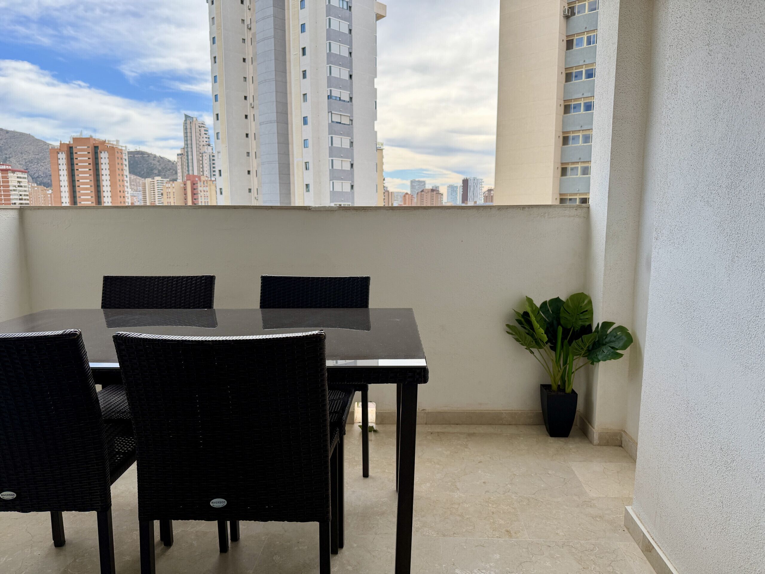 Un balcone con tavolo e sedie, una pianta in vaso e vista sulla città.