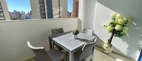 Un balcon avec une table et des chaises, un pot de fleurs et une vue sur les bâtiments de la ville.