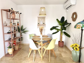 Uma sala de jantar com uma mesa redonda de vidro, quatro cadeiras, um lustre e uma planta grande.
