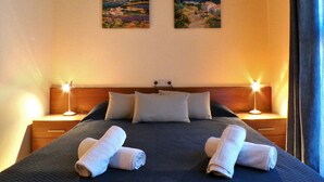 Una cama bien hecha con dos toallas enrolladas, dos lámparas de noche y dos cuadros en la pared.
