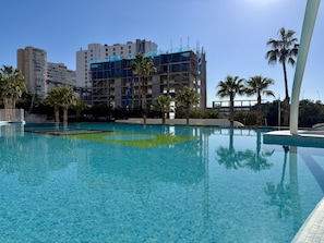 Uma piscina com água azul cristalina, rodeada por palmeiras e um edifício em construção.