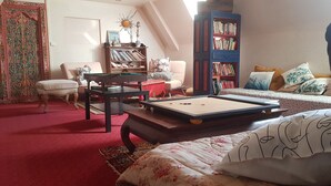 A cozy living room with a pool table, a bookshelf, a sofa, and a decorative wall piece. - La Baleine Blanche (Campan)