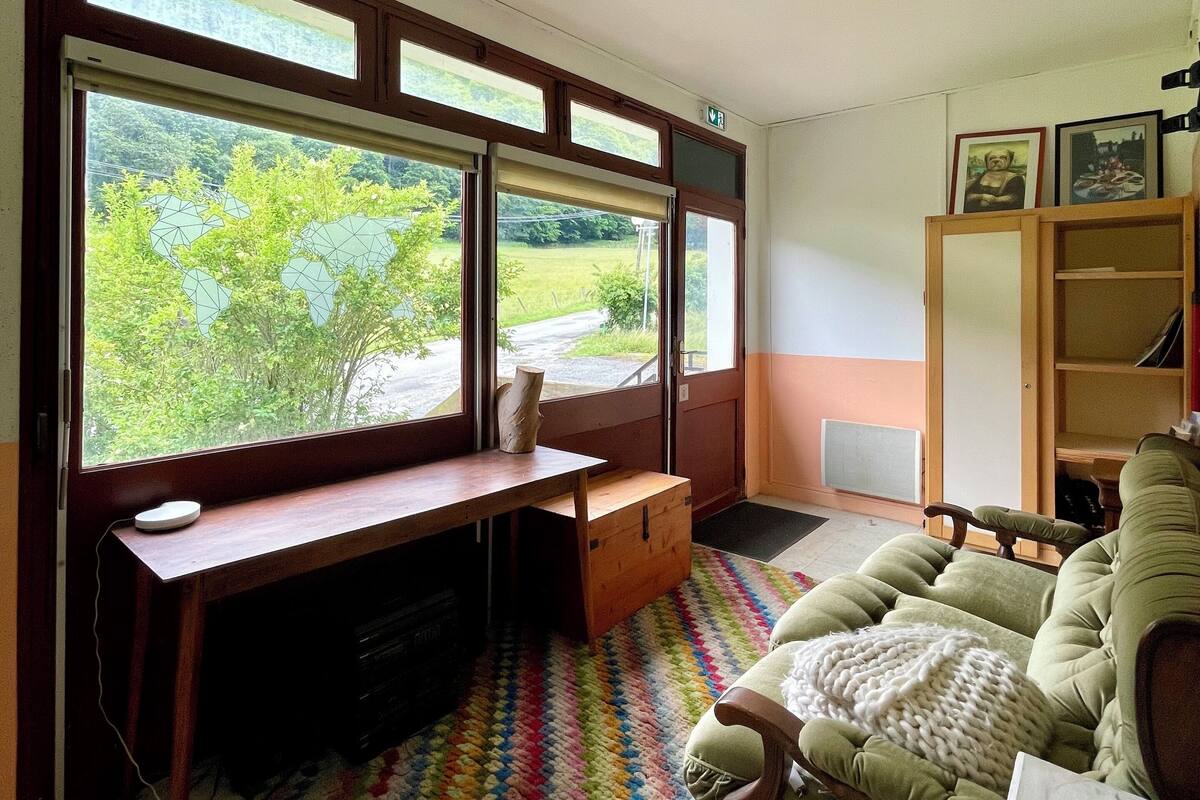 A room with large windows, a wooden desk, a green sofa, and a colorful rug.