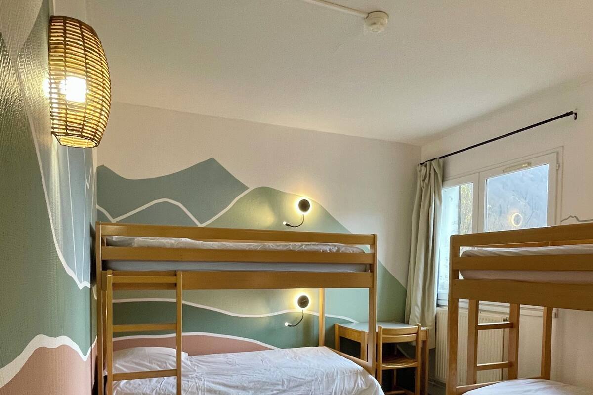 A room with three bunk beds, a small table, and a wall-mounted lamp.