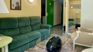 A room with a green sofa, a small table, a black speaker, and a patterned rug. - La Baleine Blanche (Campan)