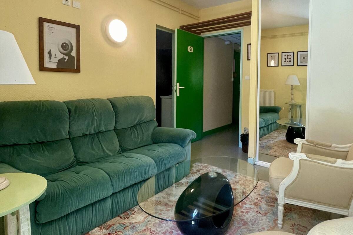 A room with a green sofa, a small table, a black speaker, and a patterned rug.