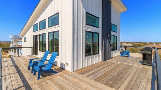 A modern house with a deck, large windows, and blue chairs. - Brand new beach house in the heart of Duck NC with sunrise and sunset views! (Duck)