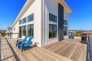 A modern house with a deck, large windows, and blue chairs. - Brand new beach house in the heart of Duck NC with sunrise and sunset views! (Duck)