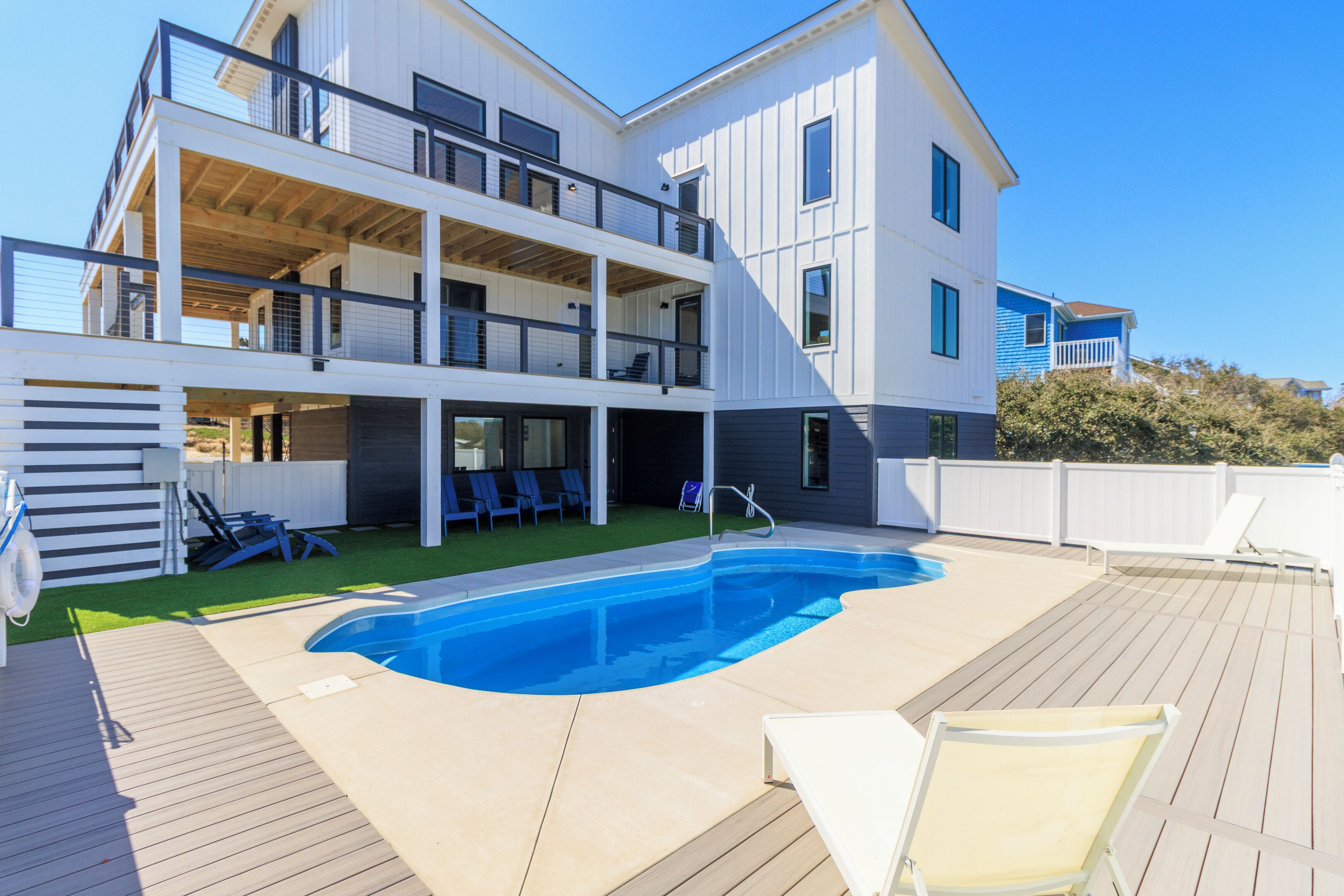 Ein zweistöckiges Haus mit Schwimmbad und Liegestühlen.