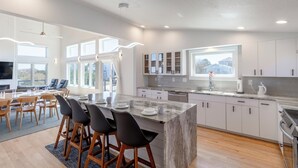 A modern kitchen with a marble island, wooden chairs, and a dining area with a large table and chairs. - Brand new beach house in the heart of Duck NC with sunrise and sunset views! (Duck)