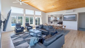 A spacious living area with a high ceiling, large windows, a modern kitchen, and a dining area. - Brand new beach house in the heart of Duck NC with sunrise and sunset views! (Duck)