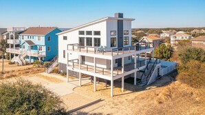 A modern two-story house with a flat roof, large windows, and a balcony. - Brand new beach house in the heart of Duck NC with sunrise and sunset views! (Duck)